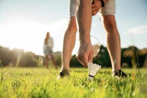 Guy is picking up the shuttlecock. Man with woman are playing badminton on ,the field photo