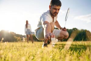 Fallen ,shuttlecock,, guy, is ,taking it. Man with woman are playing badminton on the field photo
