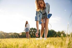 Picking ,up the fallen ,shuttlecock. Two women are having fun, with badminton rackets, on the field photo