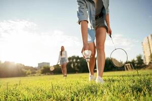 Picking up the fallen shuttlecock.. Two women are having fun, with badminton rackets, on the field photo