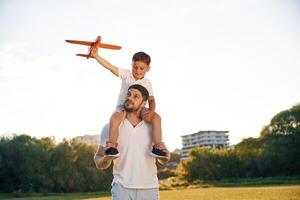 Sitting ,on man's shoulders,, with toy plane. Father and little son are together on the summer field photo