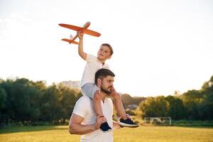 Sitting ,on,, man's ,shoulders, with toy plane. Father and little son are together on the summer field photo