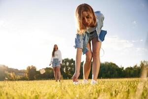 Picking ,up, the fallen shuttlecock. Two women are having fun, with badminton rackets, on the field photo