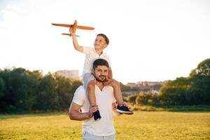 Sitting on man's, shoulders, with toy plane. Father and little son are together on the summer field photo