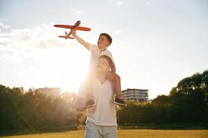 Sitting ,on, man's shoulders,,,, with toy plane. Father and little son are together on the summer field photo