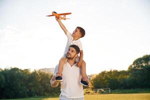 Sitting on man's shoulders,, with toy plane. Father and little son are together on the summer field photo