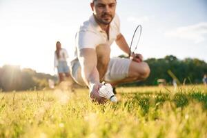 Fallen shuttlecock, guy,, is taking it. Man with woman are playing badminton on the field photo