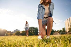 Picking, up the fallen shuttlecock. Two women are having fun, with badminton rackets, on the field photo
