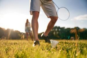 Guy is picking, up the shuttlecock. Man with woman are playing badminton on the field photo