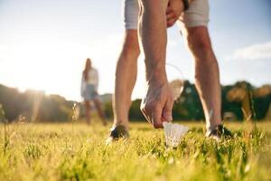 Guy, is picking up the shuttlecock. Man with woman are playing badminton on the field photo
