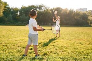 Rackets, in hands, playing badminton. Happy kids are on the summer field photo