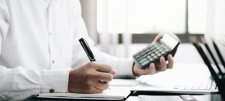 Close up Business man using calculator and laptop for do math finance on wooden desk in office and business working background, tax, accounting, statistics and analytic research concept photo