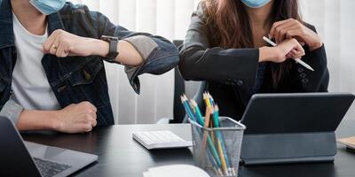 Two young diverse business colleagues wearing face protective masks bumping elbows, greeting each other while working during covid 19 quarantine. photo