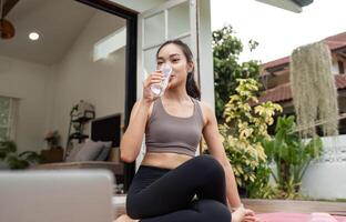 Yoga and Hydration. Young woman sipping water while practicing yoga in a serene home setting. photo