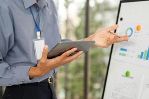 Corporate Data Review. Professional using tablet while explaining graphs on a digital board. photo