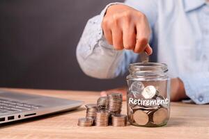 A worker putting coins into a glass jar to prepare for retirement. Saving money for retirement. photo