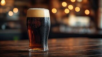 Dark beer in a glass sits on a wooden bar counter under warm ambient lights photo