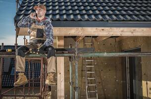 Construction Worker on Scaffolding Making a Phone Call at a Residential Building Site During the Day photo
