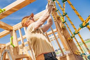 Construction of a Wooden Play Structure in a Sunny Park Setting With a Skilled Worker Assembling Climbing Ropes in the Late Afternoon photo