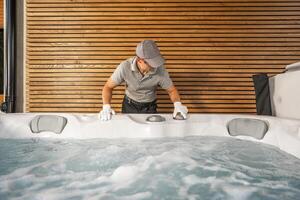 Man Cleaning Hot Tub in Modern Spa Environment With Wooden Backdrop and Bubbly Water During Daytime photo