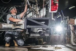 Mechanic Repairing Vehicle Undercarriage in Dimly Lit Workshop During Day photo
