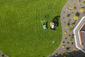 Man Mowing a Lush Green Lawn in a Well-Maintained Garden Under Bright Sunlight During Summer photo