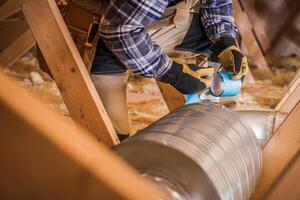 Worker Repairing Ductwork With Tape in Attic During Home Renovation Project photo