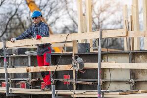Construction Worker on Scaffolding Assembling Wooden Framework at a Busy Site in Early Morning Light photo