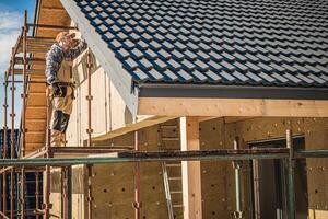 Construction Worker Installing Roof Tiles on New House Under Clear Blue Sky photo