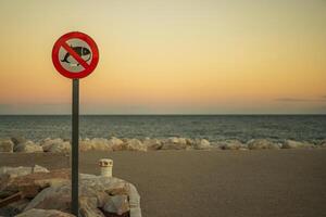 No Fishing Sign Stands on the Shore at Sunset, With Calm Waves and a Colorful Sky Reflecting the End of the Day photo