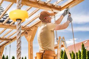Construction Worker Installs Wooden Beams on Outdoor Structure in Bright Afternoon Light While Using Ladder and Tools photo