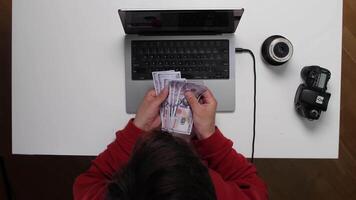 A person is sitting at a desk with a laptop and money video