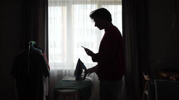 A man is standing in front of a window and using his phone video