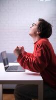 A man in glasses is sitting at a table with his laptop video