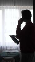 A man standing in front of a window talking on a cell phone video