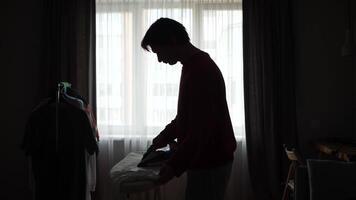 A silhouette of a man is ironing clothes in front of a window video