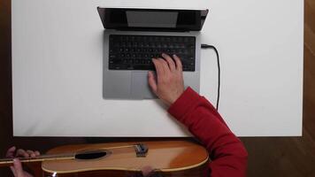A person using a laptop computer and a guitar video