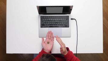 A person is holding a coin on a table with a laptop video