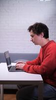 man in a red sweater is sitting at a table with a laptop video