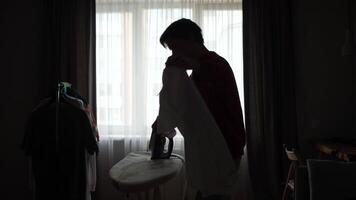 A man silhouette ironing clothes in front of a window video