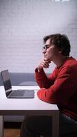 A man in glasses sits at a table with a laptop video