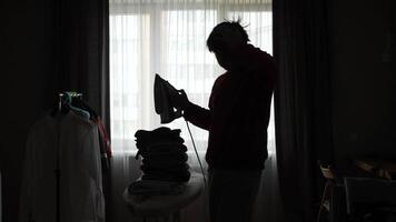 A silhouette of a man ironing clothes in a room video