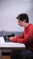 A man in a red sweater is sitting at a table with a laptop video