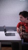 A man playing a guitar in front of a laptop video