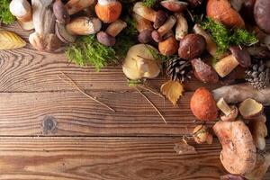 A variety of fresh forest mushrooms on a wooden background. top view, copy space. Autumn concept. Mushroom frame. photo