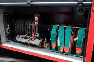 Equipment used for firefighting is neatly organized in a fire truck compartment with hoses, valves, and control panels present in the background during daylight hours. photo