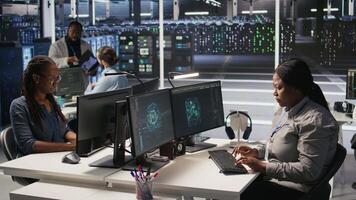 Data center system administrator using PC to monitor neural network AI visualization. African american woman in server room using computer to oversee rigs powering machine learning processes, camera A video