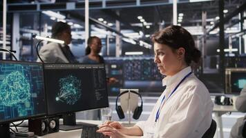 Data center software developer using PC to monitor neural network AI visualization. Woman working in server room using computer to oversee rigs powering machine learning processes, camera A video