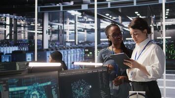 Teamworking engineers in data center integrate AI automation tools together during maintenance session. Server room colleagues configure machine learning models across server infrastructure, camera A video