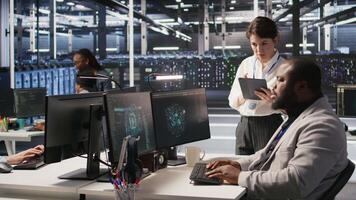 Server room manager supervise technician examining deep learning algorithms. Data center team leader and African american employee review performance dashboards of AI equipment rigs, camera A video